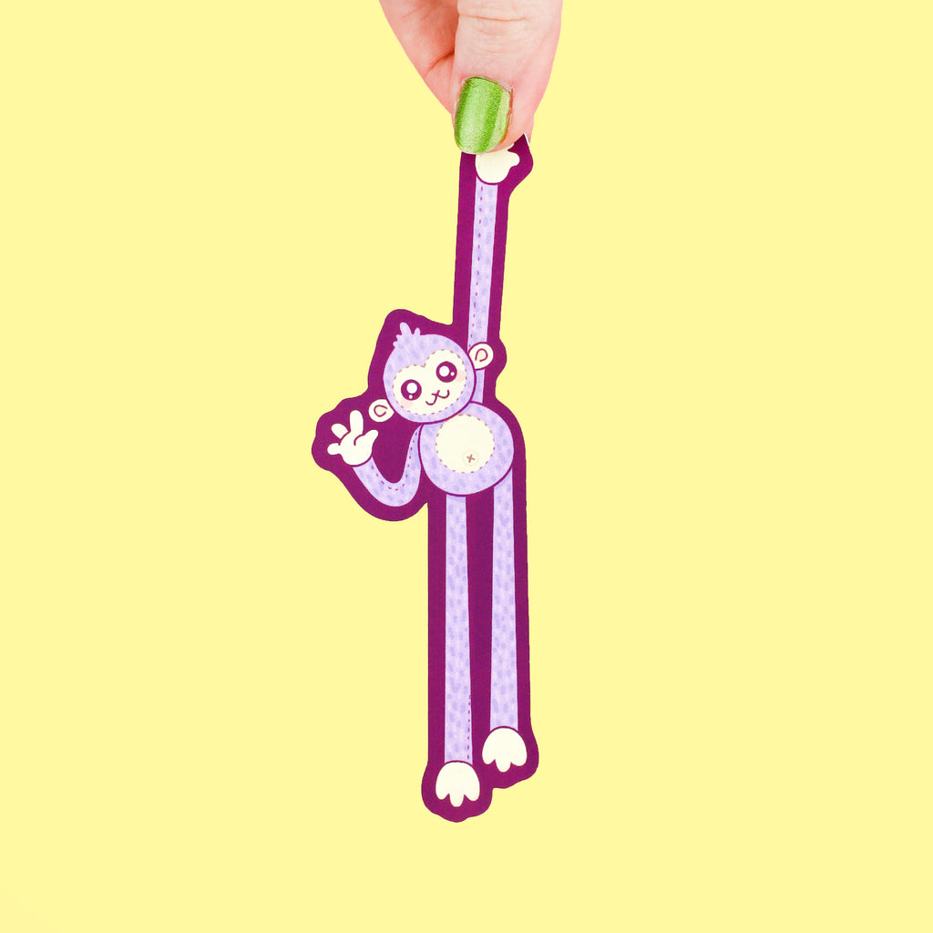 Long bookmark shaped like a monkey hanging from something high while giving a wave