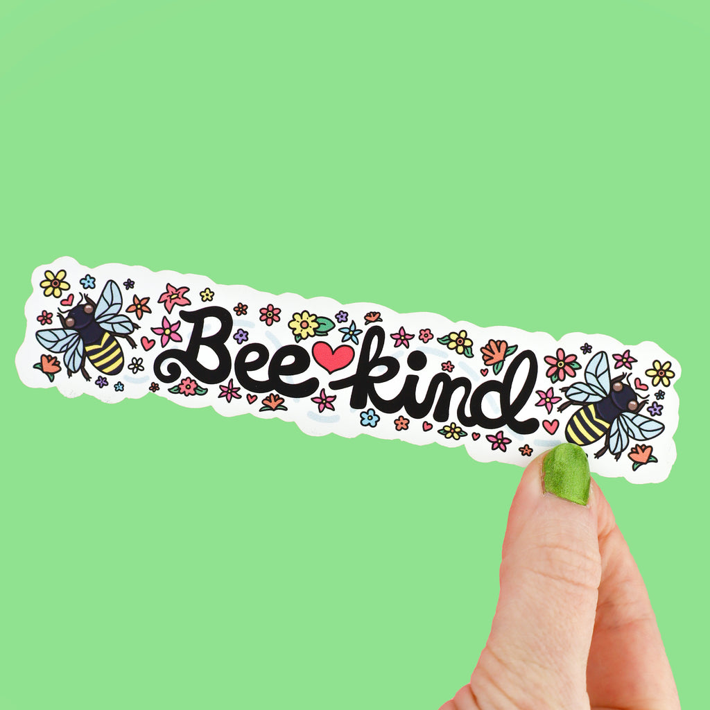 Long bookmark with white background and colorful flowers. In the center is the text 'Bee Kind' and to its side is honeybees