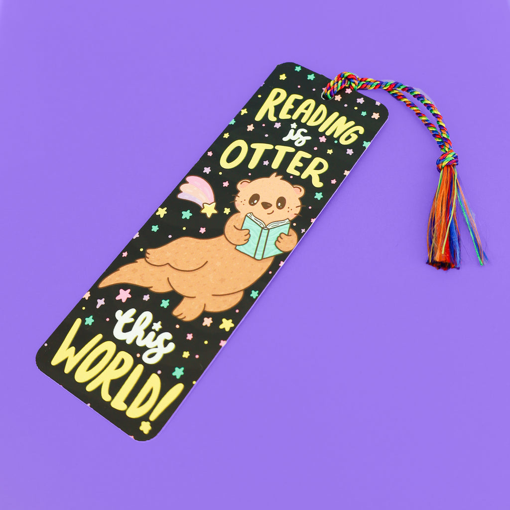 Bookmark with space background and otter reading book. Text that says "Reading is otter this world"