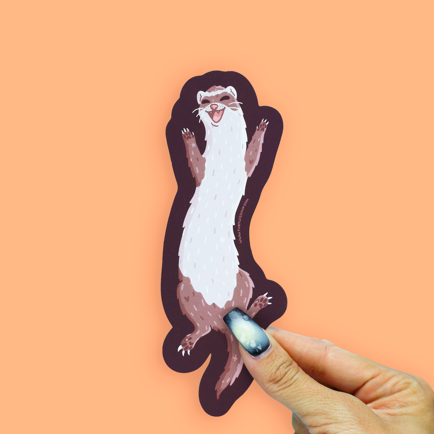 A die-cut sticker of a cartoon ferret with a dark plum outline, held by a hand against a solid peach-orange background.