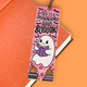 A pink Halloween-themed bookmark with a cute cartoon ghost reading a purple book, surrounded by stars, bats, pumpkins, and the text 'THIS IS A SPOOKTACULARLY GOOD BOOOOOOK!', shown resting on an orange notebook against a solid orange background.