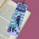 A decorative paper bookmark with a Krampus illustration and the text 'DO YOU BELIEVE IN KRAMPUS?' placed on an open book against a solid pink background.