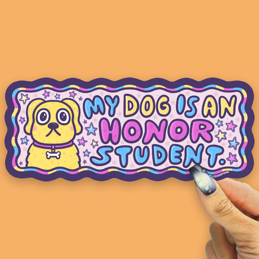 A die-cut sticker featuring a yellow cartoon dog and the text 'MY DOG IS AN HONOR STUDENT.' in colorful bubble letters, held by a hand against a solid orange background.