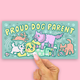 A rectangular sticker or card with a pastel illustration of playful dogs and the text 'PROUD DOG PARENT' is held by a person's hand against a solid pink background.