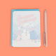 A pastel stationery set featuring a 'Season's Greetings' notepad with a snowman, penguin, and bunny illustration, shown next to a matching pink pen on a peach background.
