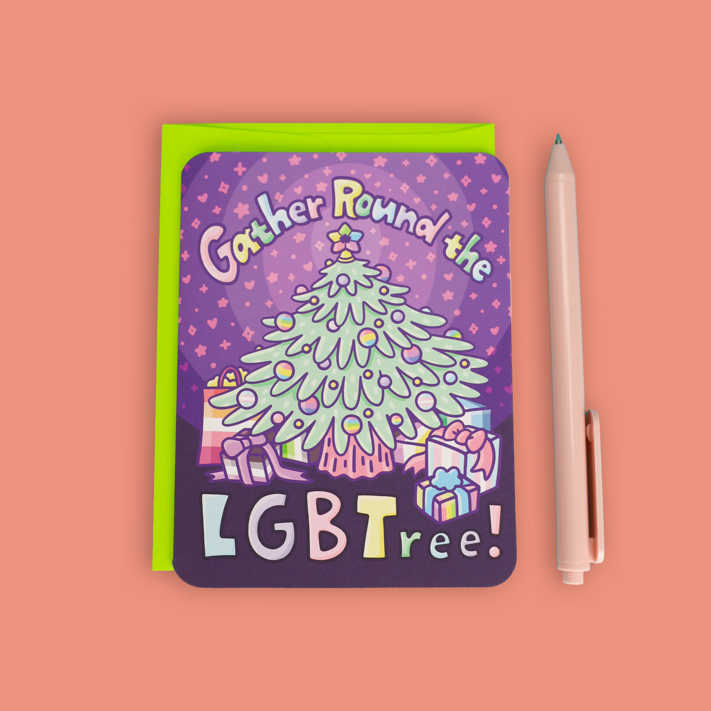 A square greeting card with rounded corners featuring a colorful illustration of a Christmas tree and the text 'Gather Round the LGBTree!' in pastel letters, shown on a peach background next to a lime green envelope and a light pink pen.