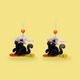 Black cat earrings against a yellow background
