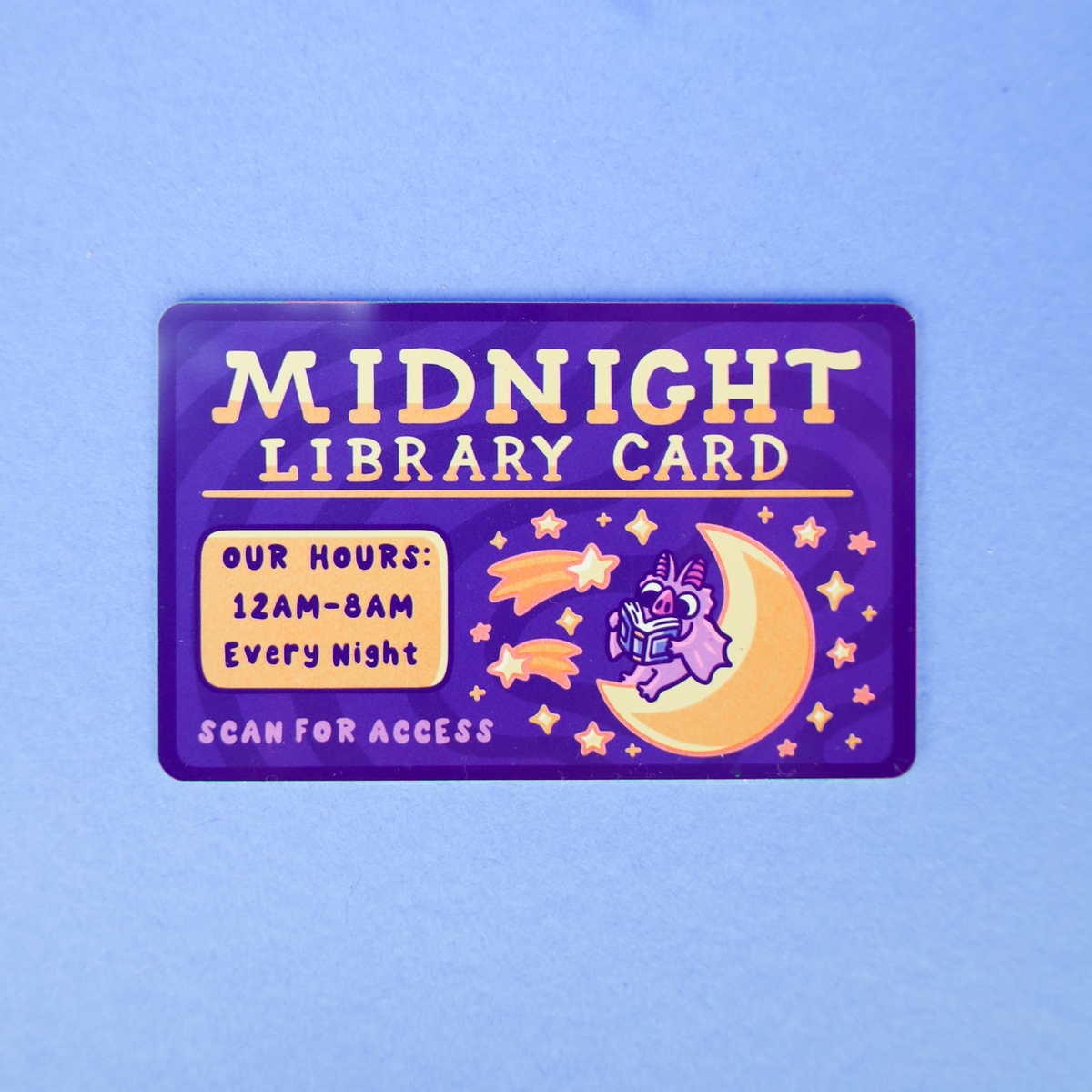 A rectangular purple card labeled 'MIDNIGHT LIBRARY CARD' with cream lettering, a yellow crescent moon and stars, and a small purple unicorn illustration, placed on a light blue background.
