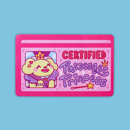 A pink rectangular sticker or card featuring a cartoon dog wearing a crown and purple outfit, with the text 'CERTIFIED Passenger Princess' on a light blue background.