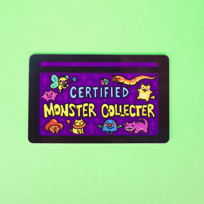 A rectangular collectible card with rounded corners featuring a purple background and cartoon monster illustrations, with the text 'CERTIFIED MONSTER COLLECTOR' in the center, shown on a light green background.