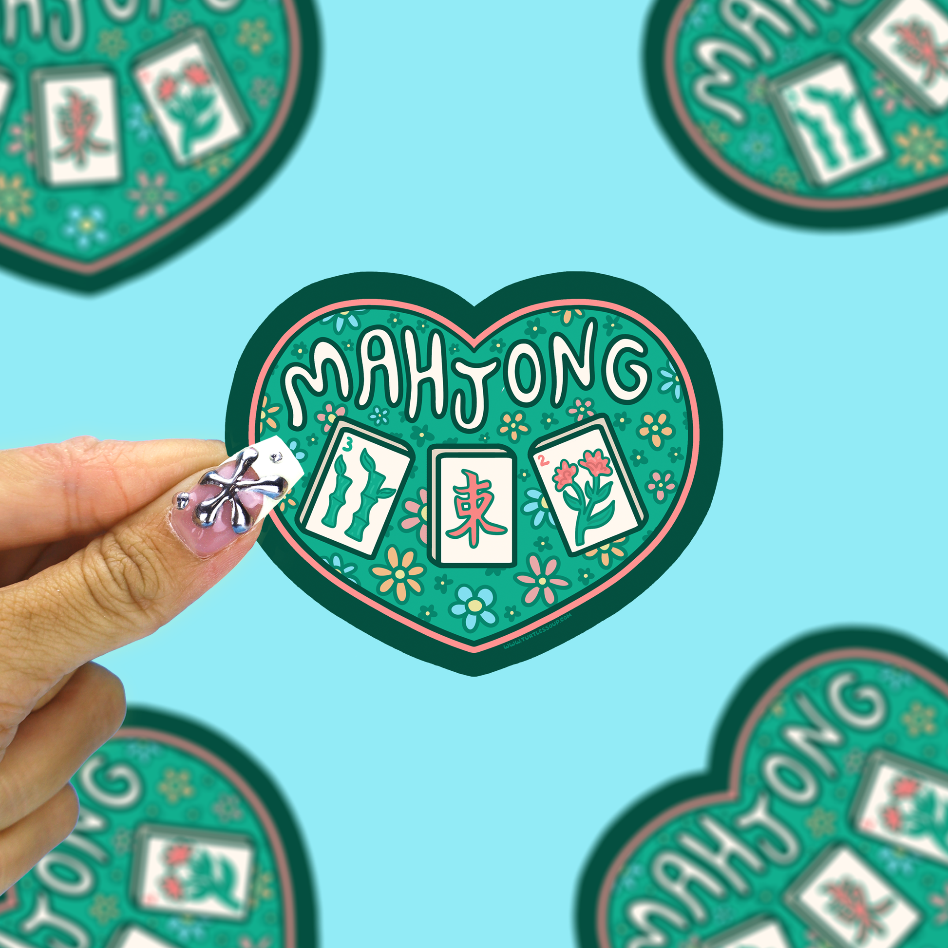 I heart mahjong vinyl sticker being held up by a hand against a blue background. 