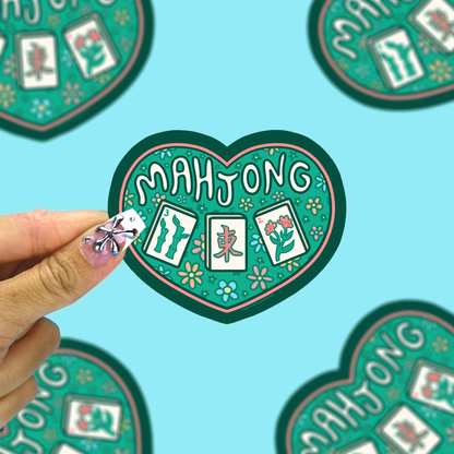 I heart mahjong vinyl sticker being held up by a hand against a blue background. 