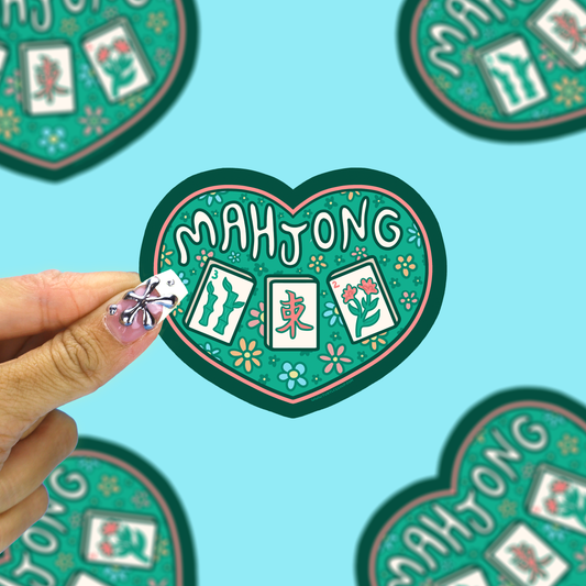 I heart mahjong vinyl sticker being held up by a hand against a blue background. 