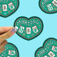 I heart mahjong vinyl sticker being held up by a hand against a blue background. 