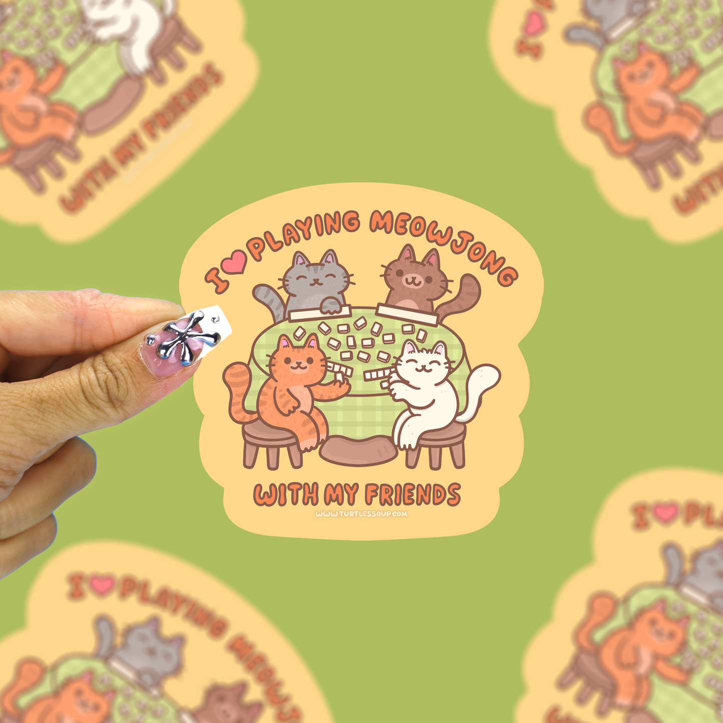 cats surrounding a table playing mahjong that says i love playing meowjong with my friends vinyl sticker being held against a green background