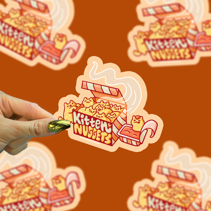 Kitten Nuggets vinyl sticker being held by a hand with a brown background