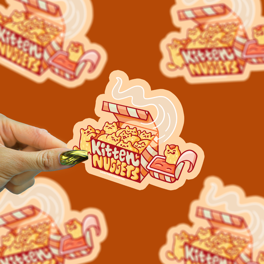 Kitten Nuggets vinyl sticker being held by a hand with a brown background