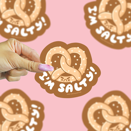 Hand holding a 'I'm Salty' pretzel-shaped sticker against a pink background with more stickers.