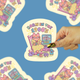 cat in a rocking chair surrounded by cute stuff from the 1990s being held against a blue background