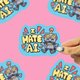 a sticker that says I hate A.I. of a robot that's RIP being held against a pink background