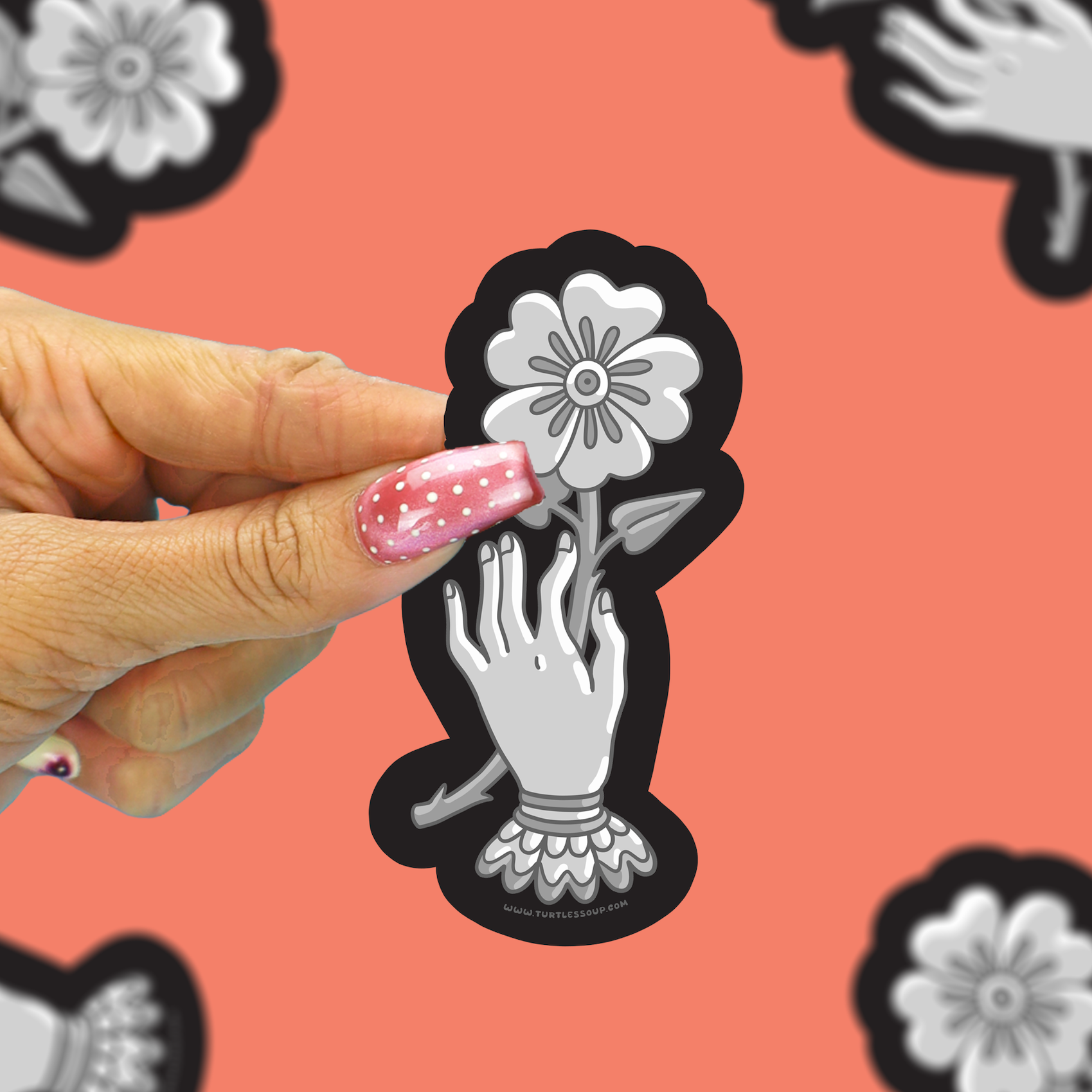 A hand with pink glitter nail polish holds a die-cut sticker featuring a black and white illustration of a hand reaching for a flower. The background is a coral pink with repeated blurred versions of the same sticker design.