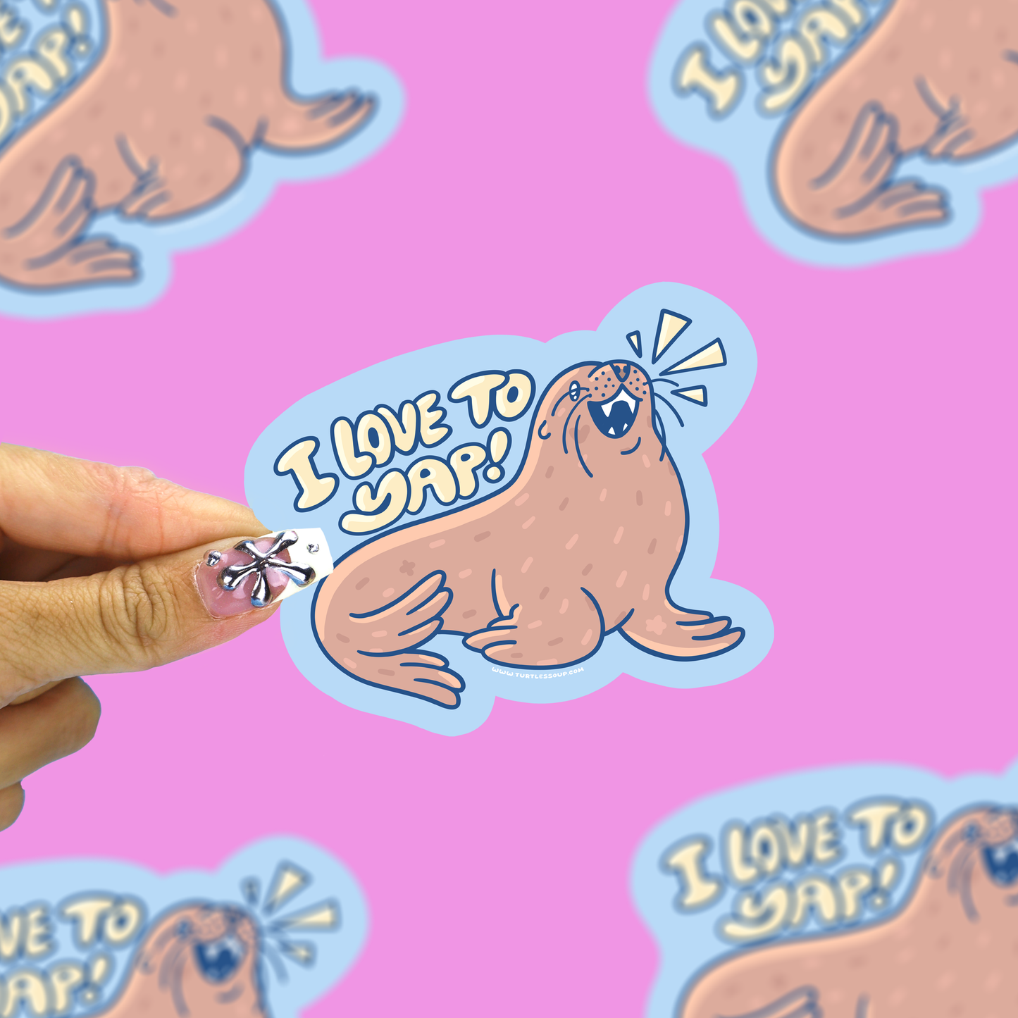 A hand with decorated nails holds a die-cut sticker featuring a cartoon walrus and the text 'I LOVE TO YAP!' on a bright pink background with repeated matching stickers.