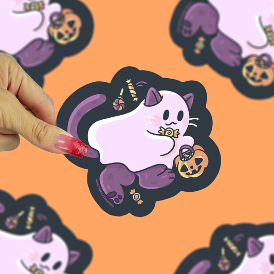 A hand with pink glittery nails holds a die-cut sticker featuring a cute white cat in purple Halloween accessories, including candy corn and a jack-o'-lantern. The background is a solid orange color with other blurred copies of the sticker.