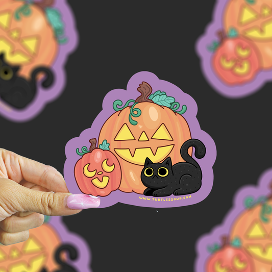 A hand with pink nails holds a die-cut sticker featuring a cartoon jack-o'-lantern, a smaller pumpkin, and a black cat on a dark background with blurred duplicate sticker images.