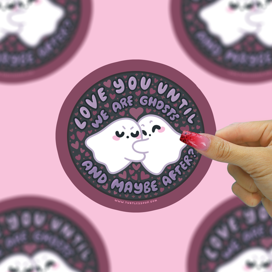 A circular sticker featuring a cute cartoon ghost illustration with the text 'LOVE YOU UNTIL WE ARE GHOSTS AND MAYBE AFTER?' is shown. A hand with red glittery nail polish is touching the sticker.