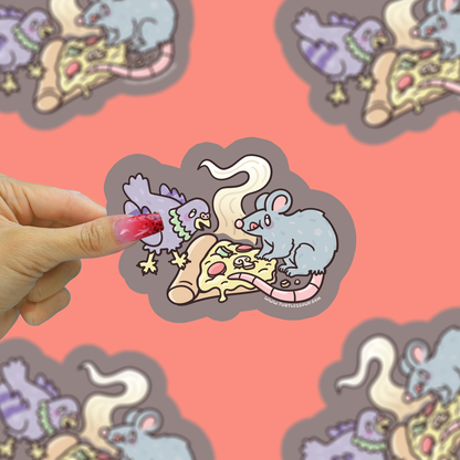 Hand holding a sticker with cartoon mice eating pizza against a patterned background