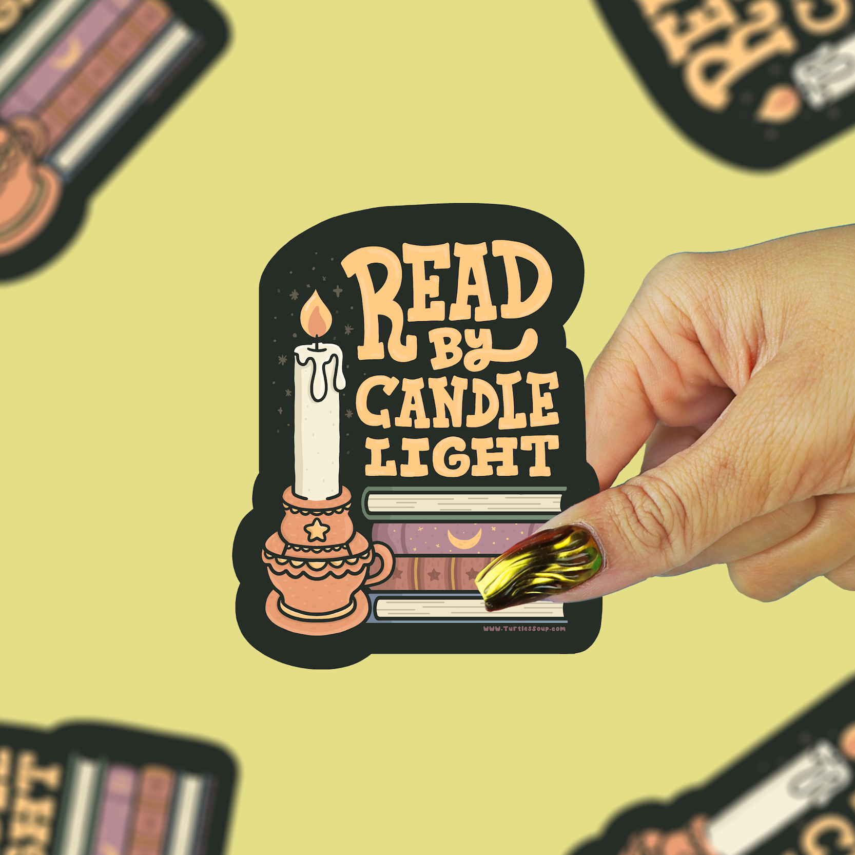 A hand with gold and green nail polish holds a die-cut sticker that reads 'READ BY CANDLE LIGHT' with an illustration of a candle and books. The background is a pale yellow with several blurred copies of the same sticker.