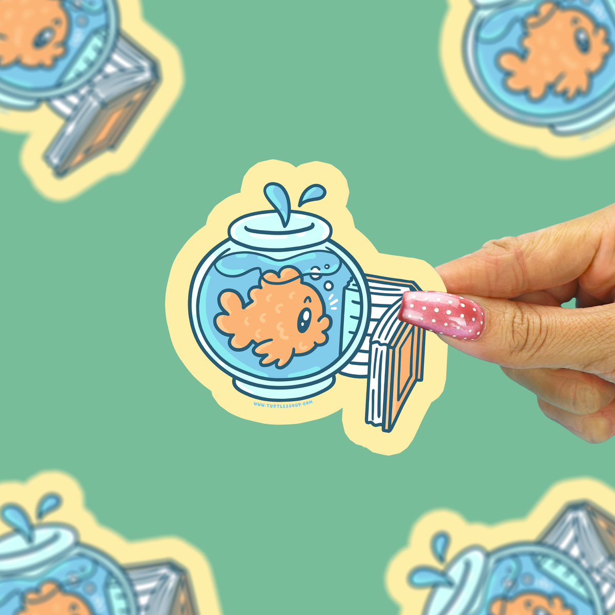 A hand with pink glitter nail polish holds a die-cut sticker featuring a cartoon goldfish in a blue fishbowl with a striped diving board. The background is a mint green patterned surface with other blurred stickers.