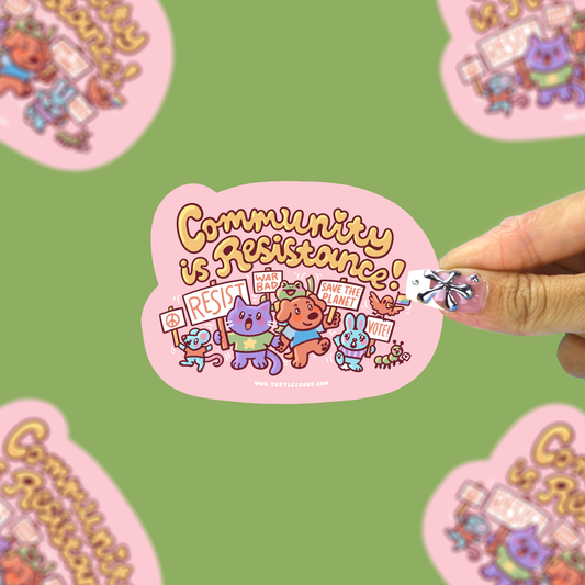 A hand holds a pink die-cut sticker featuring cartoon animals and the text 'Community is Resistance!' against a green background with blurred duplicate sticker previews.