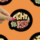 A hand with pink nail polish holds a round sticker that reads 'FIGHT FASCISM' in stylized cream and pink lettering with a green cartoon creature on a black background. The hand is centered against an orange backdrop with partial duplicate views of the same sticker around the edges.