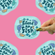 A hand holds a die-cut sticker featuring the phrase 'Friend to Fish' in dark teal lettering, surrounded by colorful cartoon fish on a light blue background. The sticker is shown against a bright pink background with other identical stickers partially visible around the edges.