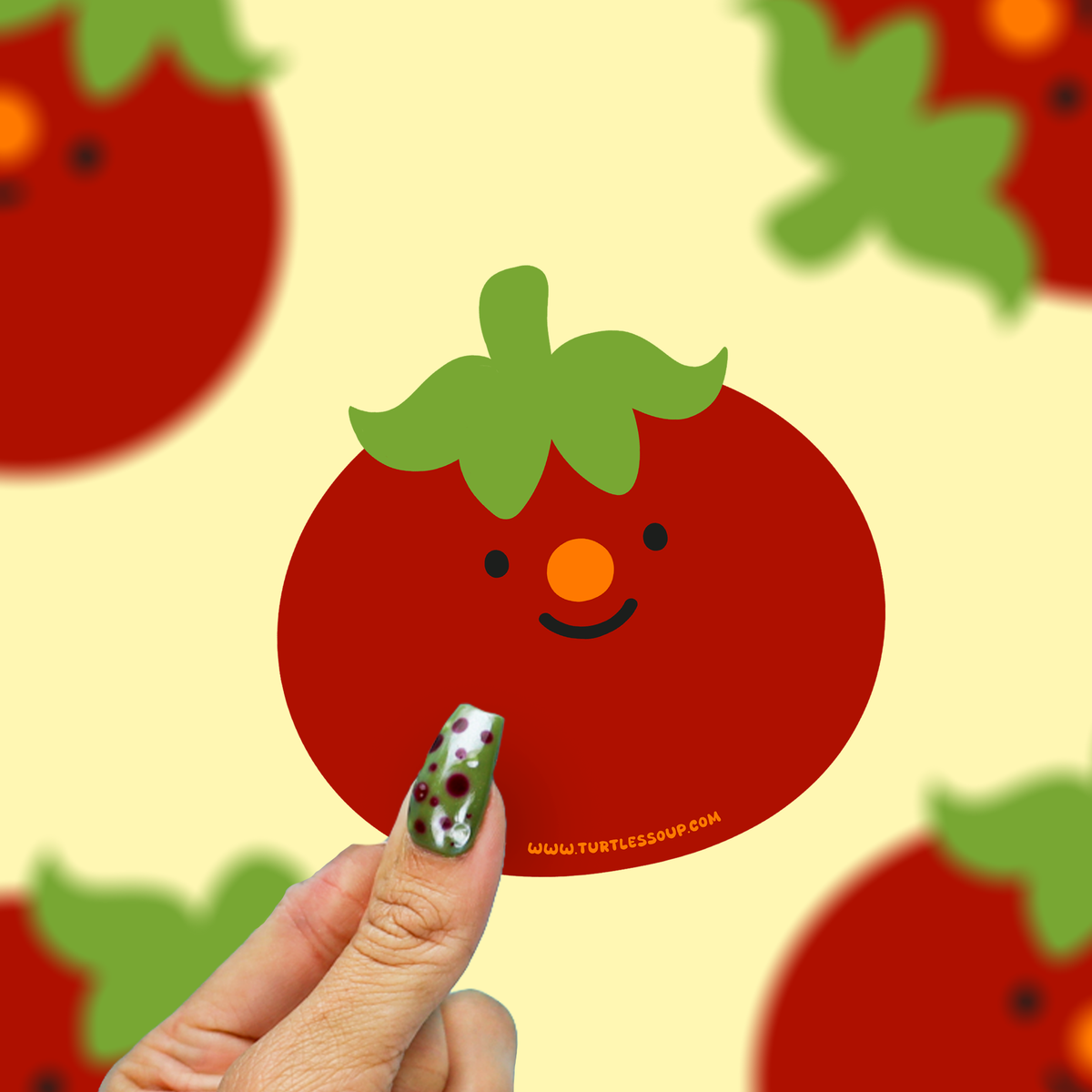 hand holding a red happy little tomato vinyl sticker against a yellow background. 