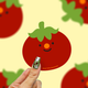 hand holding a red happy little tomato vinyl sticker against a yellow background. 