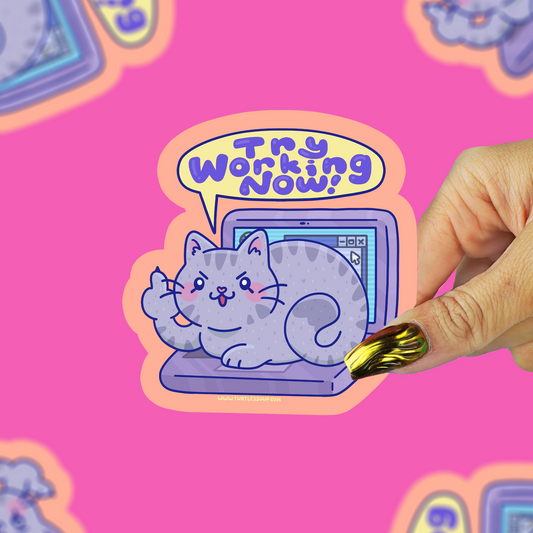 A hand with gold nail polish holds a die-cut sticker featuring a cartoon gray cat sitting on a laptop with a speech bubble that says 'Try Working Now!' against a bright pink background with repeated matching sticker designs.