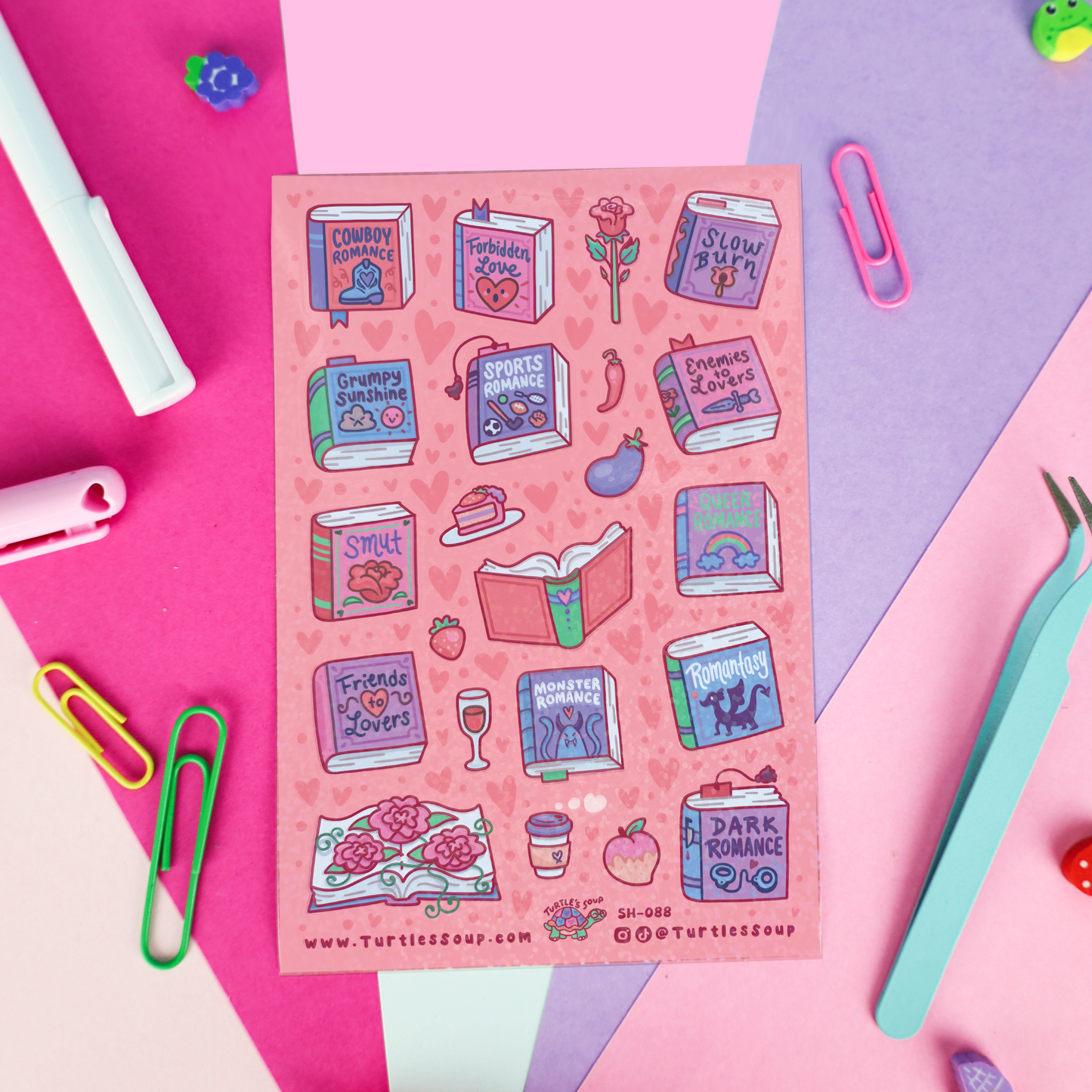 A pink sticker sheet featuring various illustrated books, quotes, and romantic-themed icons, styled on a flat-lay background of pink, purple, and blue paper with stationery props.