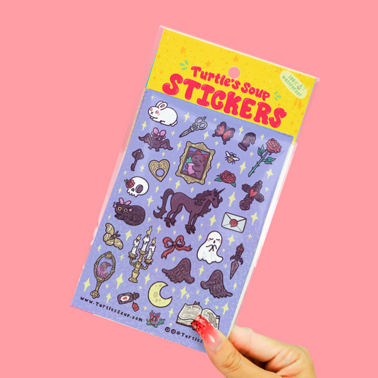 A hand with red manicured nails holds a clear plastic package of 'Turtle's Soup Stickers' against a solid pink background. The sticker sheet features various cute, spooky, and fantasy illustrations like a horse, rabbit, skull, cat, and moon on a lavender background.