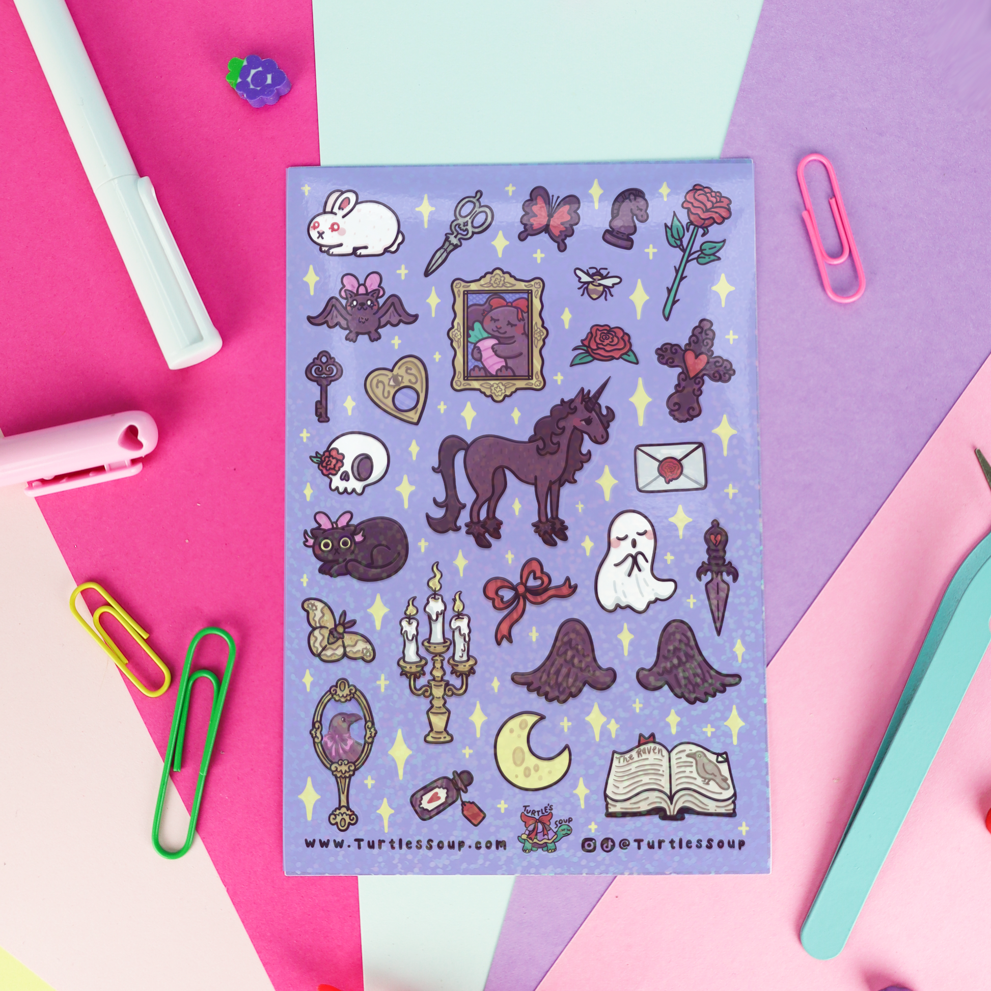 A sheet of cute gothic and Halloween-themed stickers on a lavender background, styled in a flat-lay with colorful paper clips and stationery on a pink, purple, and mint background.