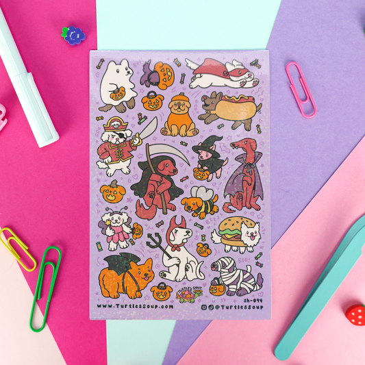 A sheet of cute cartoon pet Halloween stickers on a lavender background, surrounded by colorful paper clips, a pen, and a ruler on a pink, purple, and blue geometric paper backdrop.