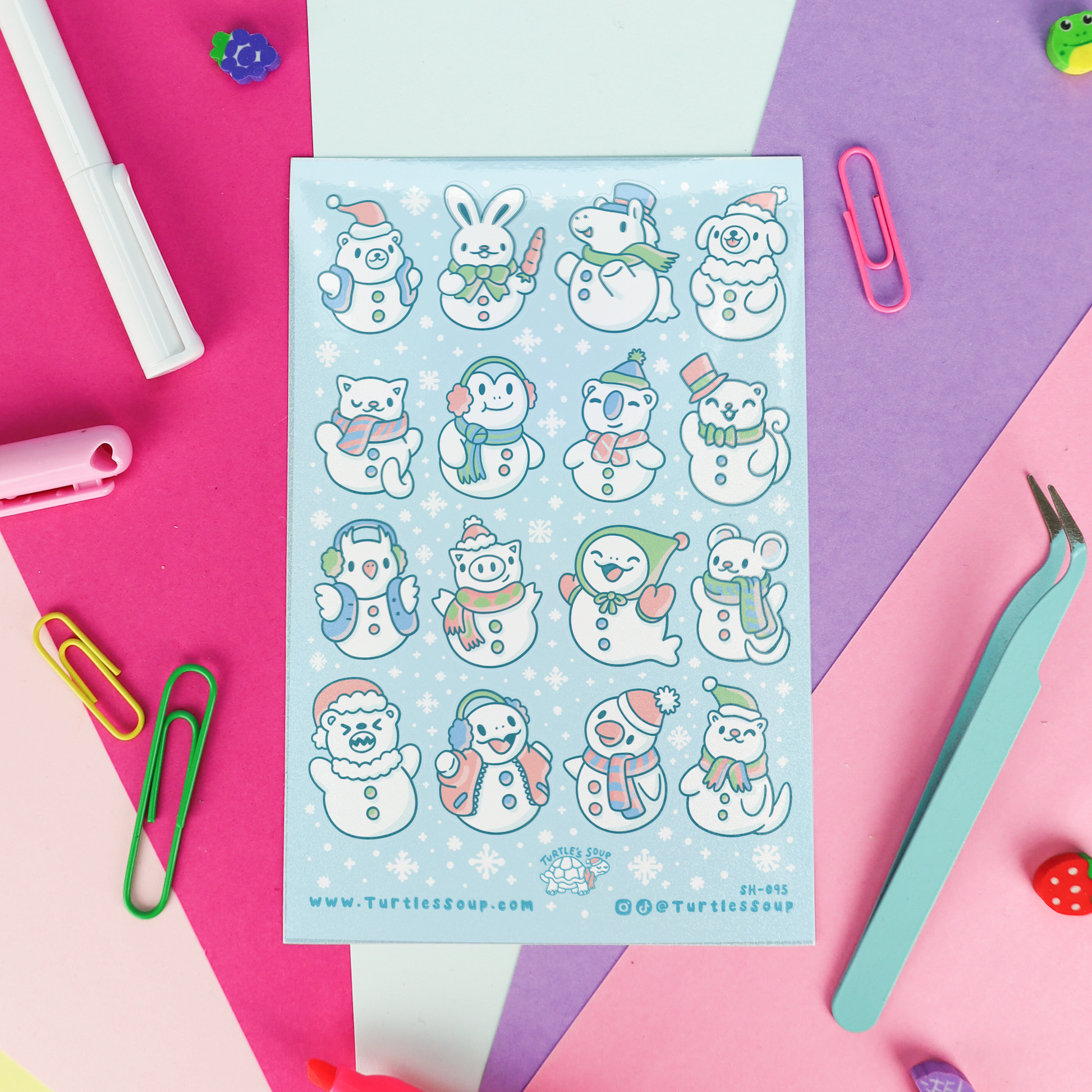 A sheet of cute cartoon snowman stickers on a pastel blue background, surrounded by colorful paper clips, tweezers, and stationery on a pink, purple, and blue geometric backdrop.