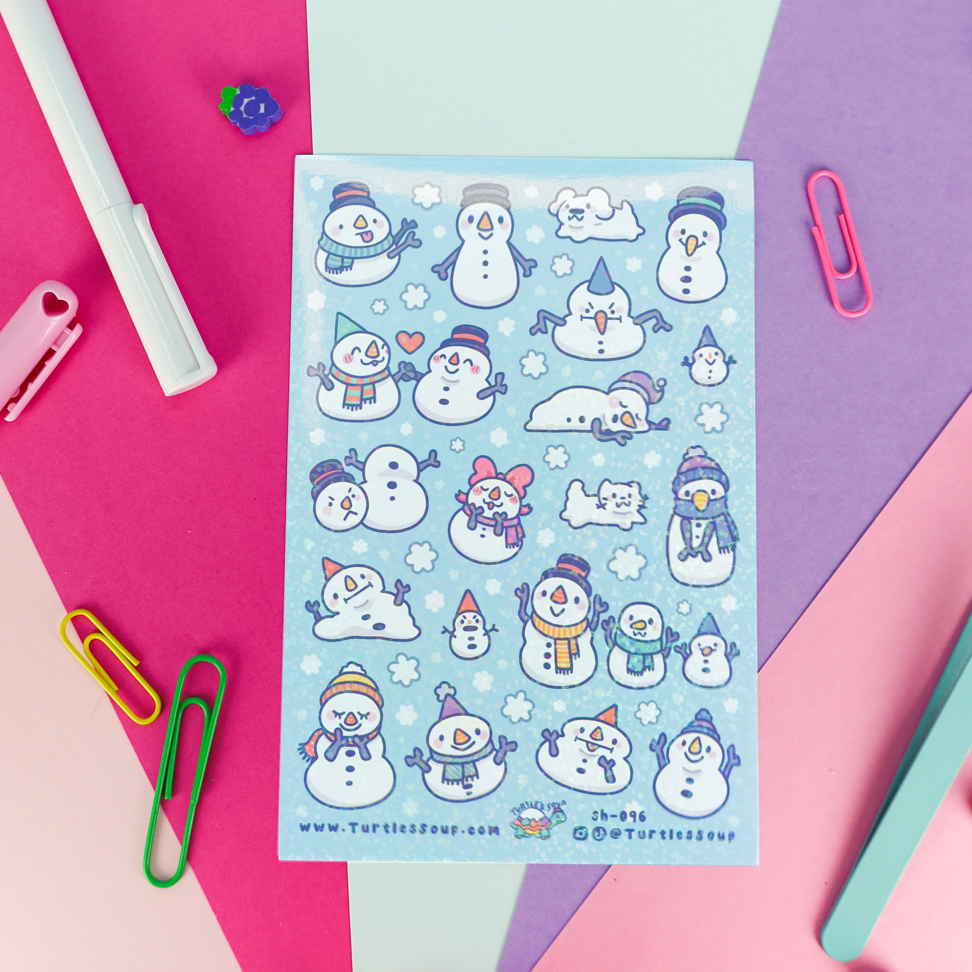 A sheet of cute winter planner stickers featuring snowmen, snow angels, and snowman cats on a light blue background, styled on a colorful pastel paper flat-lay with stationery props.