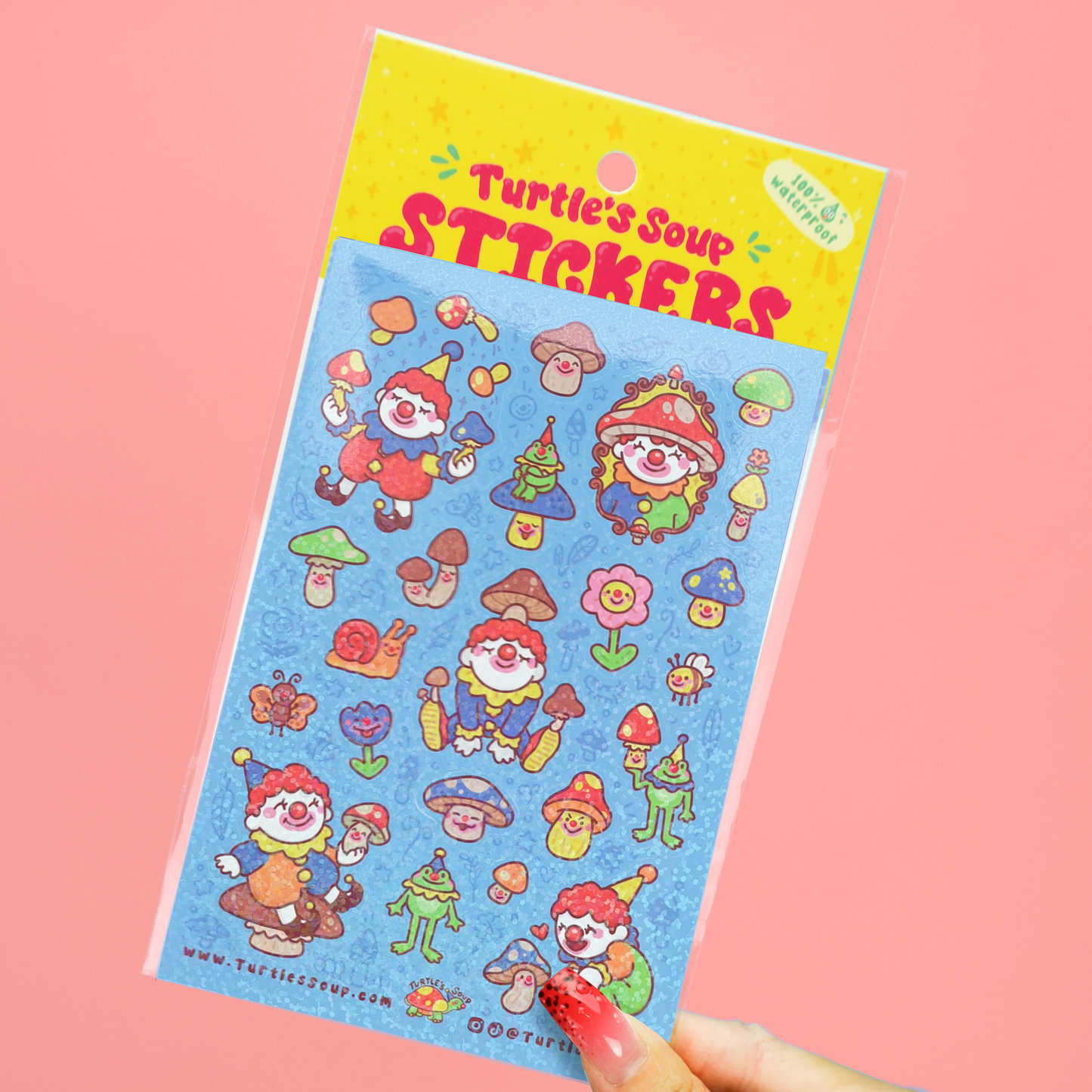 A hand holds a packaged sheet of colorful cartoon stickers labeled 'Turtle's Soup STICKERS' against a solid pink background. The sticker sheet has a blue background with whimsical characters, mushrooms, flowers, and tools in bright red, green, yellow, and orange.