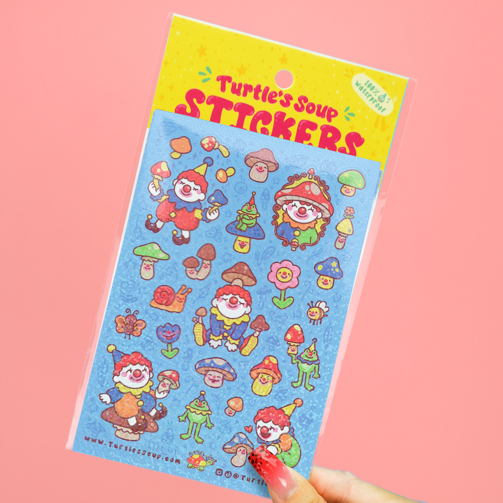 A hand holds a packaged sheet of colorful cartoon stickers labeled 'Turtle's Soup STICKERS' against a solid pink background. The sticker sheet has a blue background with whimsical characters, mushrooms, flowers, and tools in bright red, green, yellow, and orange.