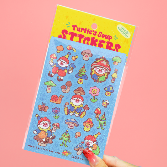 A hand holds a packaged sheet of colorful cartoon stickers labeled 'Turtle's Soup STICKERS' against a solid pink background. The sticker sheet has a blue background with whimsical characters, mushrooms, flowers, and tools in bright red, green, yellow, and orange.